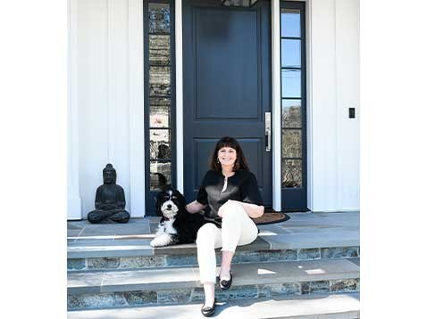 A smiling woman sitting on the front porch with a dog